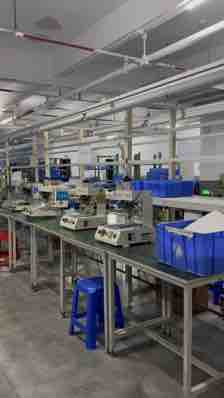 Factory assembly area with workstations and blue work-in-process bins